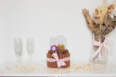 Foto de Concepto romántico. Pastel de chocolate con dos vasos vacíos, ramo de flores secas en la mesa blanca - Imagen libre de derechos