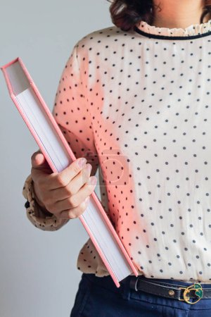 Téléchargez les photos : Plan recadré d'une jeune femme tenant un livre rose - en image libre de droit