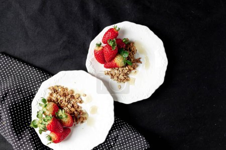 Photo for Strawberries for breakfast. Strawberries with granola and honey on a white plates and black background. - Royalty Free Image