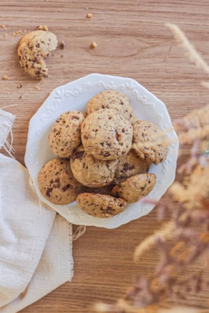 Téléchargez les photos : Vue du dessus de délicieux biscuits dans une assiette en céramique avec tissu de lin et fleurs séchées sur une table en bois - en image libre de droit