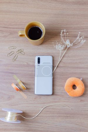 Photo for Female home office desk workspace with a cup of coffee, pen, washi tapes, string, paper clips, wild flowers and a smartphone on a wooden table. - Royalty Free Image