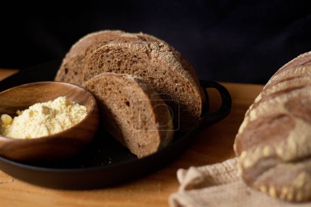 Photo for Sliced brown bread with flour in bowl on wooden table. Dark composition. Bakery concept. - Royalty Free Image
