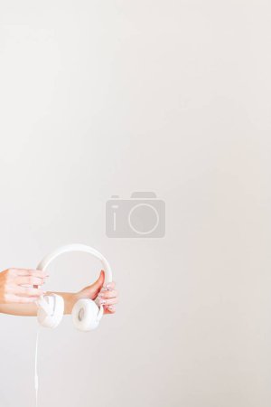 Photo for Female hand holding a white headphone. Minimalist concept. - Royalty Free Image