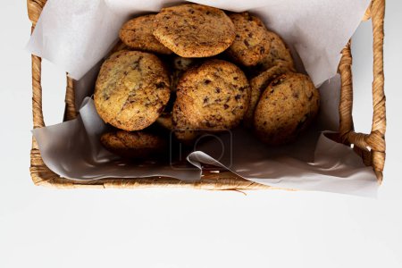 Téléchargez les photos : Vue rapprochée de biscuits faits maison dans un panier de paille avec du papier parchemin sur fond blanc - en image libre de droit