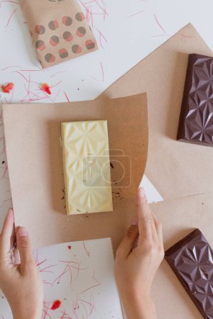 Foto de Manos femeninas envolviendo barra de chocolate en papel artesanal. Concepto de estilo de alimentos. - Imagen libre de derechos