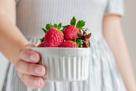 Photo for Young woman in a striped dress holding strawberries. - Royalty Free Image