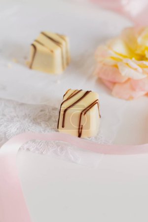 Photo for Delicious white chocolate candies and pale pink ribbon on white background. - Royalty Free Image