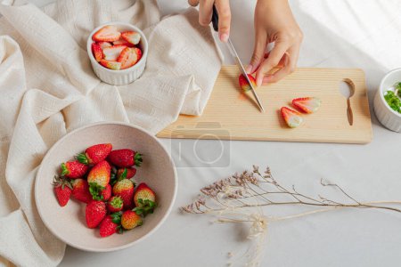 Téléchargez les photos : Jeunes mains féminines coupant quelques fraises sur planche à découper sur fond stylisé. - en image libre de droit