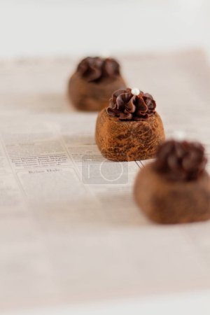 Téléchargez les photos : Trois bonbons au chocolat sur fond de journal. Stylisme alimentaire. - en image libre de droit