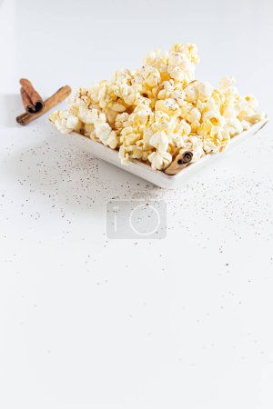 Photo for Popcorn pile in white bowl decorated with cinnamon stickes on white background - Royalty Free Image
