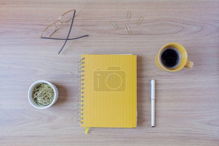 Foto de Área de trabajo de escritorio de oficina doméstica femenina con una taza de café, planificador amarillo, vasos, bolígrafo y clips de papel en la mesa de madera. Piso tendido, vista superior. - Imagen libre de derechos