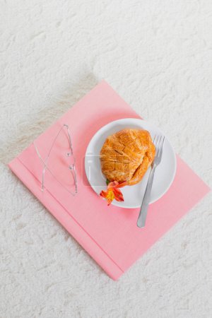 Photo for Morning breakfast with croissant on white plate, pink photo album and eyeglasses on white background - Royalty Free Image