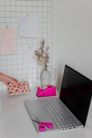 Téléchargez les photos : Esthétique minimaliste bureau à domicile espace de travail. Jeune femme utilisant un cahier pendant le travail. Ordinateur portable et fournitures de papeterie sur bureau blanc. Concept d'entreprise - en image libre de droit