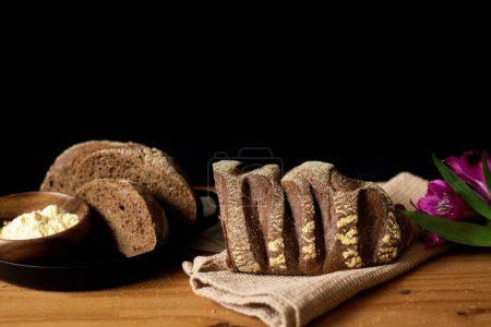 Foto de Pan integral y rebanado en una mesa de madera.Decorado con flores. Composición oscura. Concepto de panadería. - Imagen libre de derechos