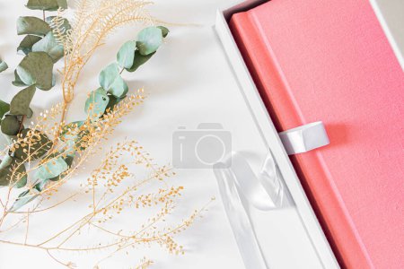 Foto de Álbum de fotos rosa con flores secas y hojas de eucalipto en sábana blanca - Imagen libre de derechos