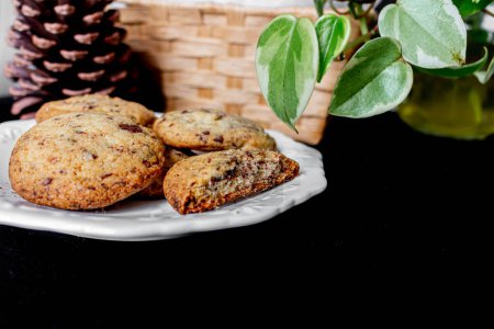 Téléchargez les photos : Biscuits sur une assiette, pin, panier de paille, feuilles de plantes sur fond noir. - en image libre de droit