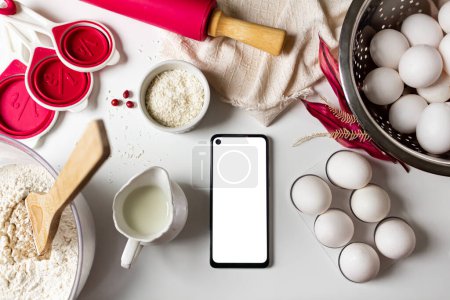 Photo for Bake a cake concept. Ingredients and kitchen utensils and blank screen mobile phone on white background. Flat lay, top view. - Royalty Free Image