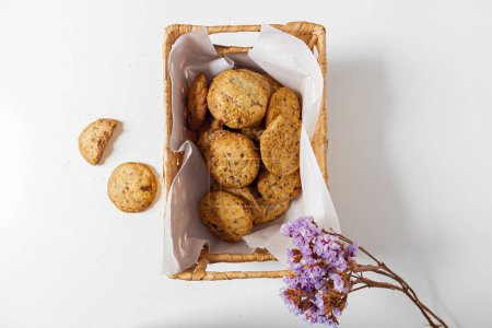Téléchargez les photos : Vue du dessus des biscuits dans un panier de paille avec des fleurs séchées sur fond blanc - en image libre de droit