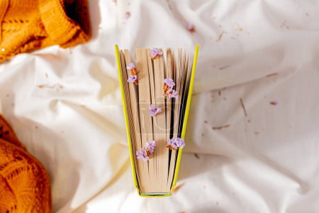 Téléchargez les photos : Automne, composition d'automne. Un livre sur le drap de lit blanc, avec des fleurs minuscules lilas séchées à travers les pages. Couché plat, vue du dessus. - en image libre de droit