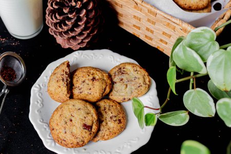 Téléchargez les photos : Biscuits sur une assiette, pin, verre de lait, panier de paille, feuilles de plantes sur fond noir. - en image libre de droit