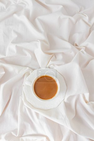 Photo for Top view of cup of coffee with milk on a messy bed. Breakfast composition. - Royalty Free Image