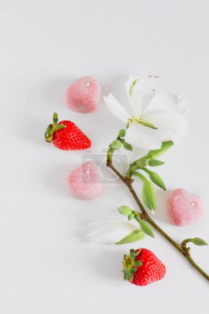 Foto de Composición de alimentos de primavera con ramas de flores, fresas y caramelos sobre fondo blanco - Imagen libre de derechos