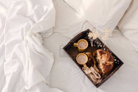 Téléchargez les photos : Petit déjeuner sur plateau vintage en bois foncé au lit avec drap beige clair et oreillers. concept matin romantique. - en image libre de droit