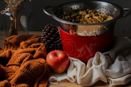 Photo for Autumnal bake a apple cake concept. Sliced apples in metal colander with brown sweater and pine cone on wooden table - Royalty Free Image