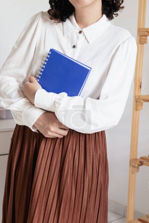 Téléchargez les photos : Jeune jolie femme en jupe plissée, chemise blanche tenant un carnet sur fond blanc. Mode vintage inspiré look vêtements. - en image libre de droit
