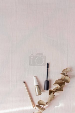 Téléchargez les photos : Accessoires de style féminin : mascara, vernis à ongles, crayon pour les yeux doré et eucalyptus sur fond blanc. - en image libre de droit