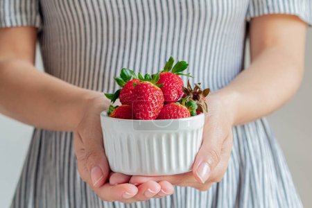 Photo for Young woman in a striped dress holding strawberries. - Royalty Free Image