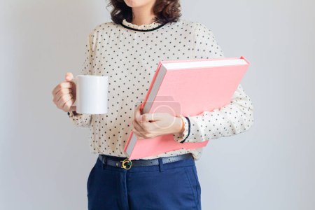 Téléchargez les photos : Plan recadré d'une jeune femme tenant une tasse blanche et un album rose - en image libre de droit