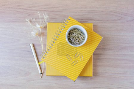 Foto de Planificadores amarillos con clips de papel en la parte superior y flores silvestres y pluma a un lado en la mesa de madera. oficina en casa escritorio espacio de trabajo - Imagen libre de derechos