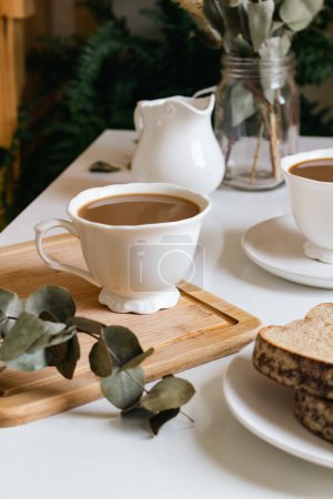 Foto de Concepto de desayuno matutino con tazas de café, pan y ramas secas de eucalipto - Imagen libre de derechos