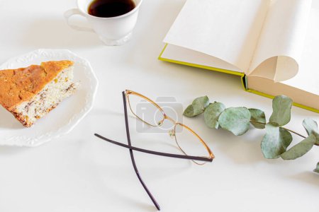 Téléchargez les photos : Composition du petit déjeuner du matin avec livre, lunettes, morceau de gâteau et tasse de café - en image libre de droit