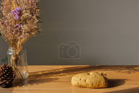 Foto de Pieza de pan fresco, cono de pino y ramo de flores secas en jarrón sobre mesa de madera - Imagen libre de derechos