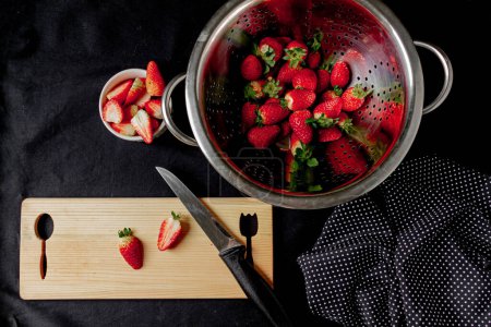 Photo for Strawberries in a bowl, some strawberries cut on the cutting board, on a black background. - Royalty Free Image