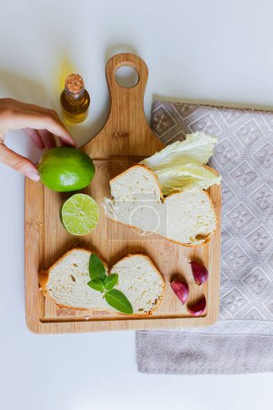 Foto de Plato mediterráneo con aceite de oliva y pan. Mano femenina sosteniendo lima sobre tabla de madera con rebanadas de pan - Imagen libre de derechos
