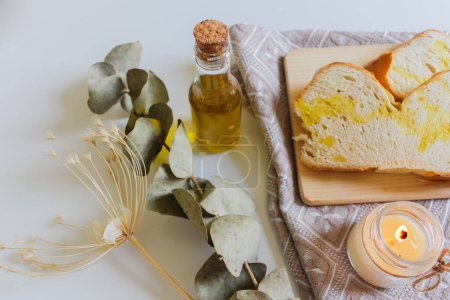 Photo for White bread slices with olive oil on the top on wooden board with candle and an eucalyptus dried leaves - Royalty Free Image