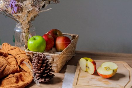 Téléchargez les photos : Composition automnale avec pommes vertes tranchées sur planche de bois, panier de paille avec pommes rouges et cône de pin un pull marron - en image libre de droit