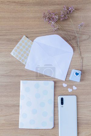 Photo for Envelope on wooden table. Artist home office desk workspace with smartphone, notebook, heart paper cutter, wild flowers and stationery. - Royalty Free Image