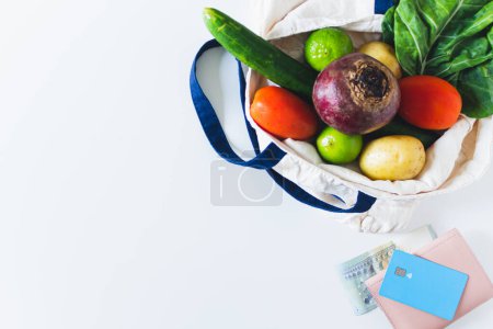 Foto de Vista superior de la bolsa ecológica llena de verduras frescas y tarjeta de crédito con billetera en blanco - Imagen libre de derechos