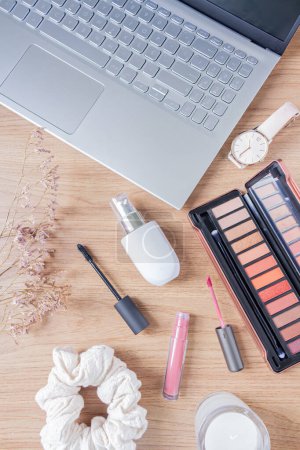 Photo for Beauty blog fashion concept. Female styled accessories: laptop, scrunchie, wildflowers and cosmetics on wooden background. Flat lay, top view trendy feminine background. - Royalty Free Image