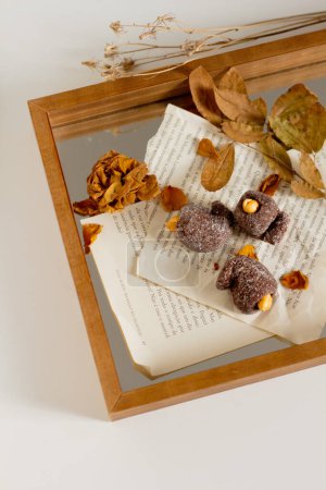 Photo for Aesthetic autumn composition. Chocolate candies on paper with dried leaves on wooden tray - Royalty Free Image