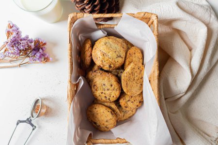 Téléchargez les photos : Vue du dessus des biscuits faits maison dans un panier de paille avec lait et fleurs séchées de côté - en image libre de droit