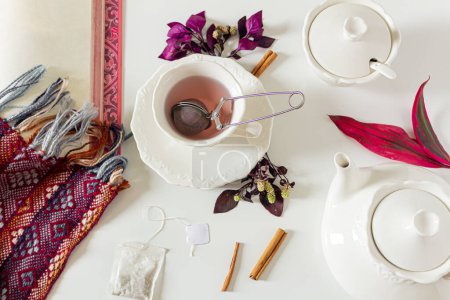 Foto de Copa de composición de té de jengibre con hojas púrpura y rosa, canela, colador de té, bolsa de té sobre fondo blanco. Asiento plano, vista superior. Concepto de hora del té. - Imagen libre de derechos
