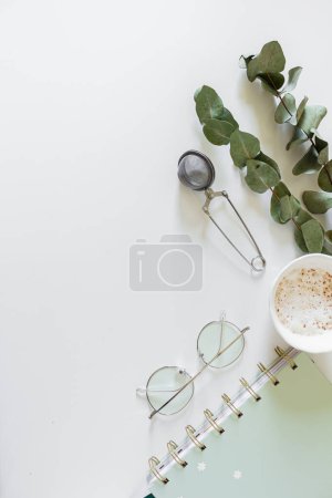 Foto de Planificador, taza de café y leche, hojas de eucalipto, vasos, colador de té sobre fondo blanco. Plano, vista superior, espacio para copiar. - Imagen libre de derechos