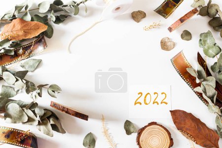 Photo for Card hand written 2022. Frame with old-fashioned camera films, dried branches of eucalyptus leaves, and wood pieces on white background. Flat lay, overhead view, top view. Vintage composition. - Royalty Free Image