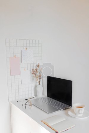 Téléchargez les photos : Concept d'entreprise. Bureau à domicile minimaliste avec ordinateur portable, tasse de thé et fournitures fixes - en image libre de droit
