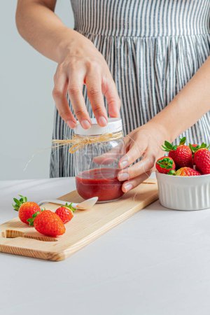 Téléchargez les photos : Jeune main féminine tenant un pot de confiture de fraises. - en image libre de droit